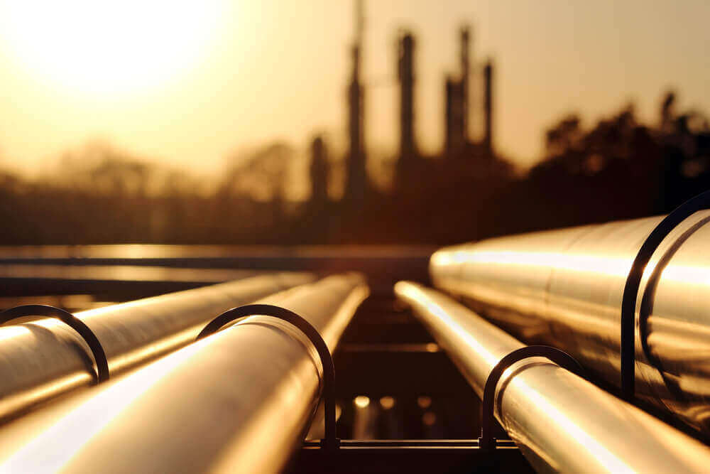 oil pipes with a silhouette view of a refinery